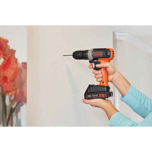 Photo of BLACKDECKER BCD702C1 cordless drill in use, drilling into a white wall indoors.