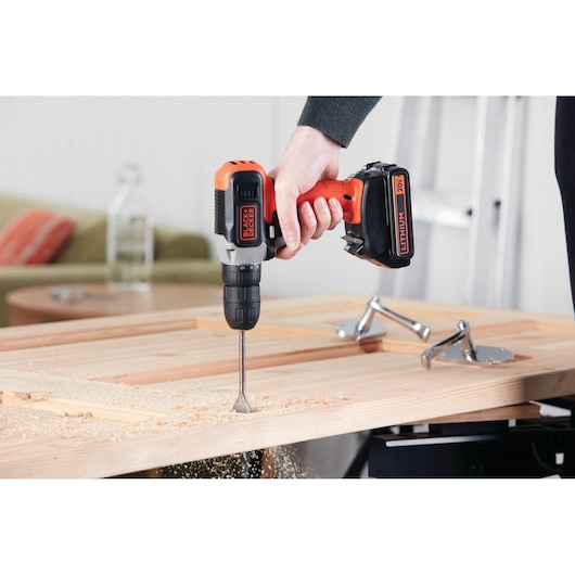 Photo of BLACK+DECKER cordless drill BCD702C1 drilling into a wooden board indoors.