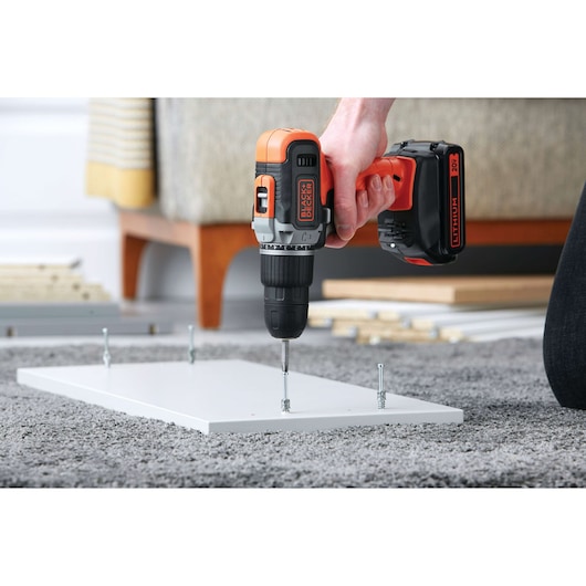 Photo of BLACKDECKER cordless drill BCK21S1S being used to drive screws into a white wooden board on carpet.