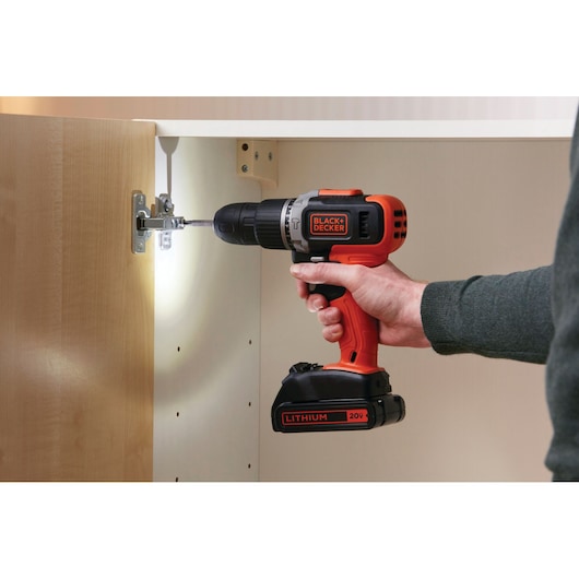 BLACKDECKER BCK21S1S cordless drill used on cabinet hinge, orange and black, close-up side angle.