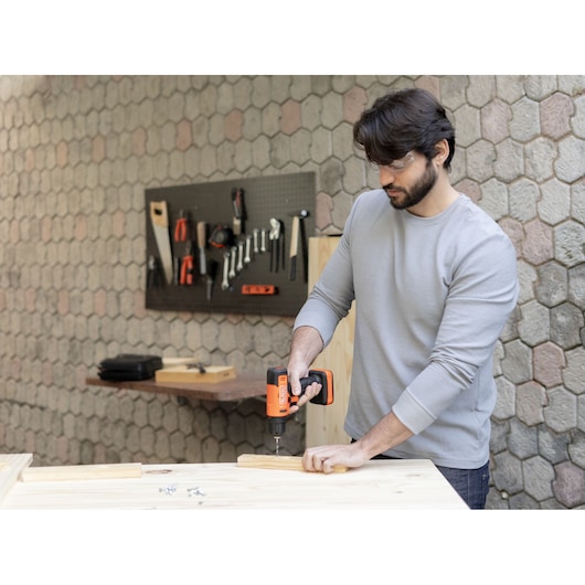Photo of BLACKDECKER BCD712VHD cordless drill in use assembling wood in a workshop, tools visible on wall rack.