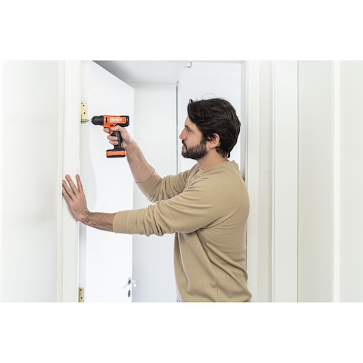 Photo of person using BLACKDECKER BCD712VHD cordless drill on door hinge, indoor scene.