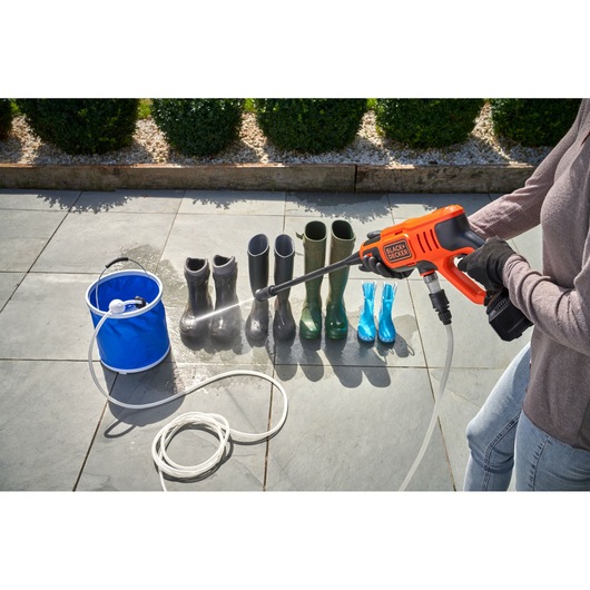 BLACKDECKER BCPC20D1 portable power washer spraying boots on patio, bucket and hose visible.