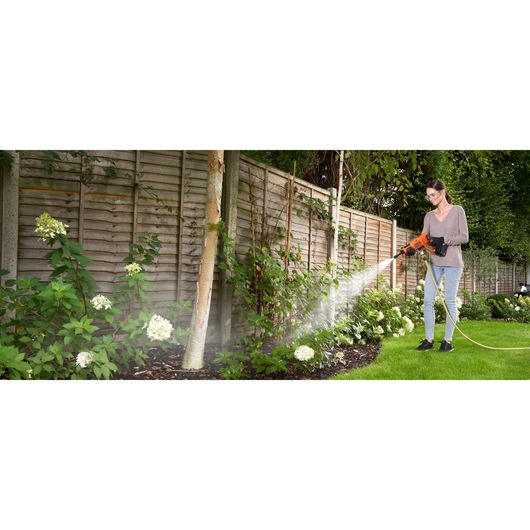 BLACKDECKER BCPC20D1 pressure washer used outdoors on garden plants by a person.