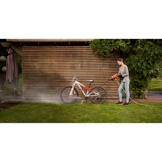 BLACKDECKER BCPC20D1 pressure washer cleaning a white and red bicycle outdoors on grass.