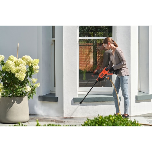 BLACKDECKER BCPC20D1 cordless pressure washer cleaning outdoor patio near white house and potted flowers.