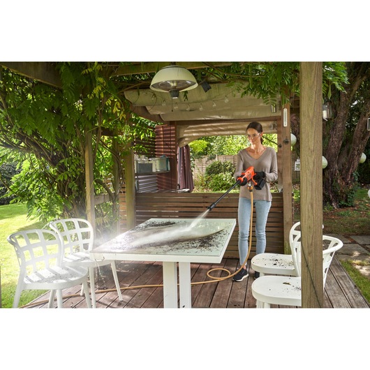 BLACKDECKER BCPC20D1 pressure washer cleaning outdoor table in garden setting.
