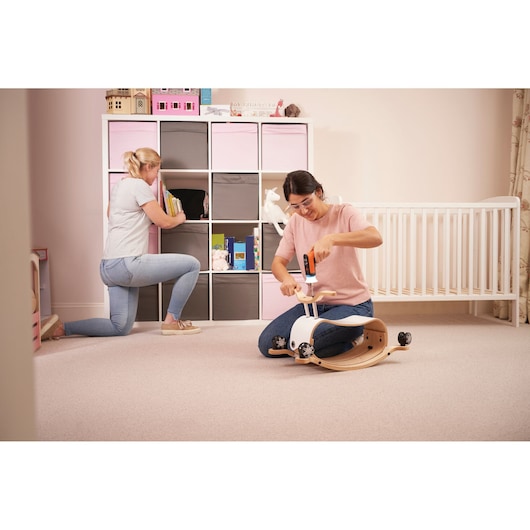 BLACKDECKER BCRTA601I cordless screwdriver in use assembling a child's wooden rocker toy in a nursery room, side angle.