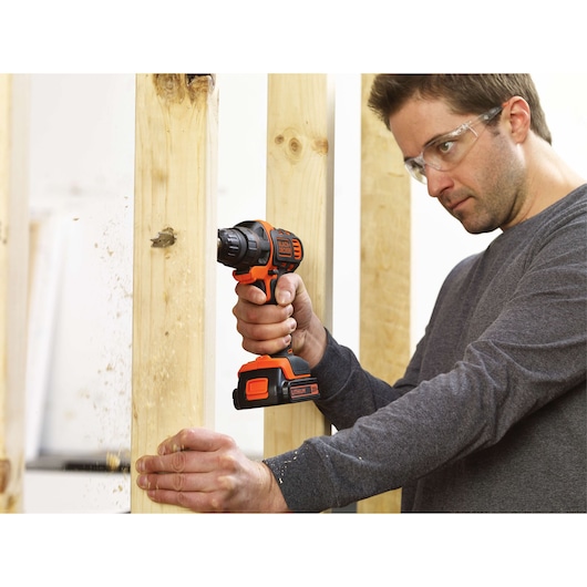 Photo of a person drilling into wood with a BLACKDECKER cordless drill BDCDM6KITC, close-up on tool in use.