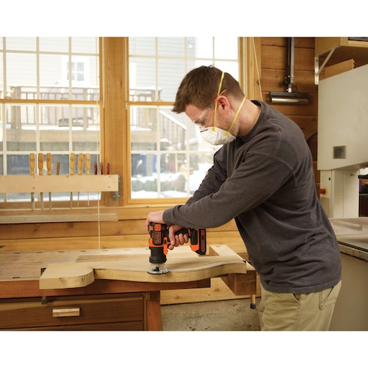 Person using BLACKDECKER BDCDM6KITC cordless drill on a wooden board in a workshop.