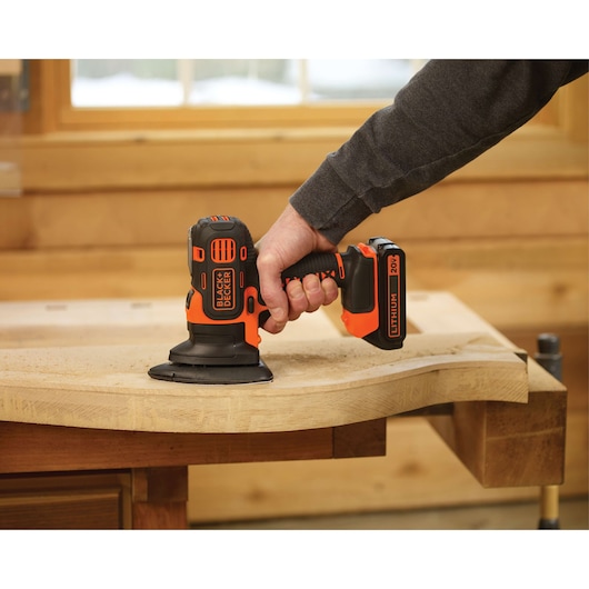 Photo of BLACKDECKER BDCDM6KITC cordless sander in use on a wooden workpiece indoors.