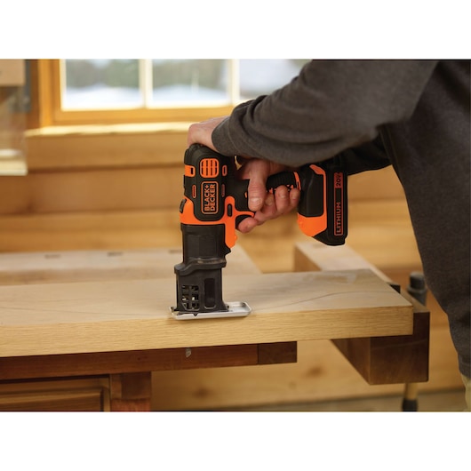 BLACKDECKER BDCDM6KITC cordless jigsaw in use cutting wood on a workbench in a workshop.