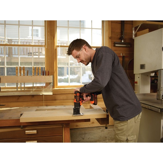 Person using BLACKDECKER BDCDM6KITC cordless drill on wooden board in workshop.