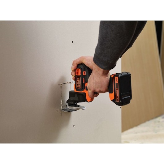 BLACKDECKER BDCDM6KITC cordless oscillating multi-tool cuts drywall panel, close-up of tool in use.