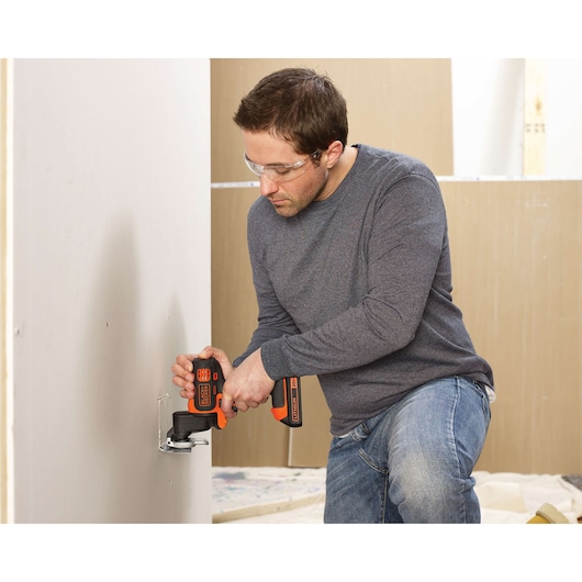 Photo of a person using a BLACKDECKER BDCDM6KITC cordless multi-tool to cut drywall.