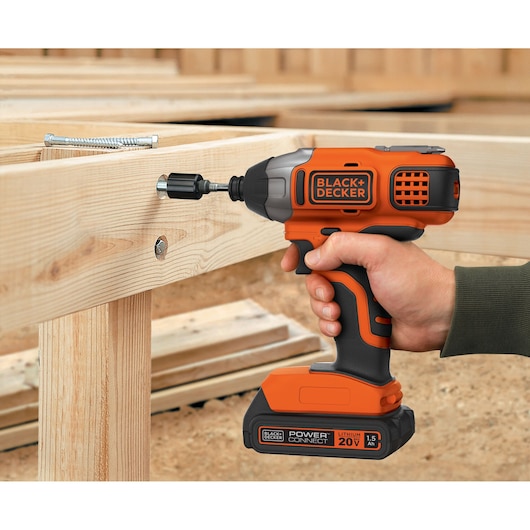Photo of BLACK+DECKER BDCI20C cordless impact driver in use on wood frames, orange and black design, handheld.