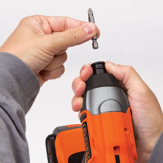Photo of hands inserting a screwdriver bit into a BLACKDECKER BDCI20C cordless impact driver, close-up view.
