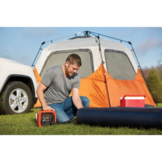 Photo of BLACKDECKER BDINF12 inflator being used outdoors near a tent and cooler, inflating an air mattress.