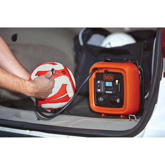 BLACK+DECKER BDINF12 portable inflator in car trunk inflating a red and white soccer ball, close-up view.