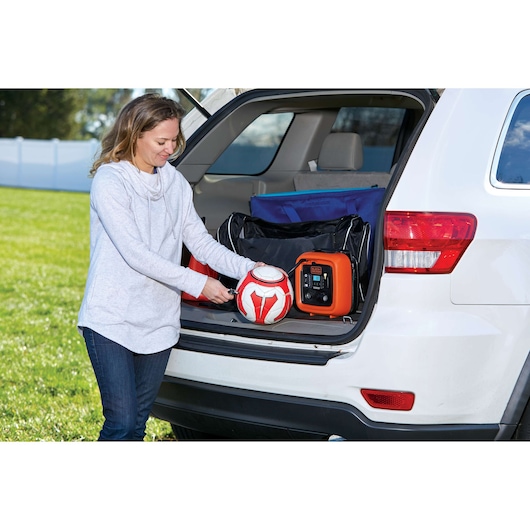 BLACKDECKER BDINF12 inflator in SUV trunk inflating a red and white soccer ball outdoors.