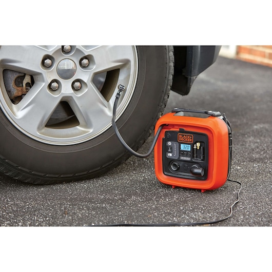 BLACK+DECKER BDINF12 portable inflator connected to a car tire in use on asphalt, angled view.