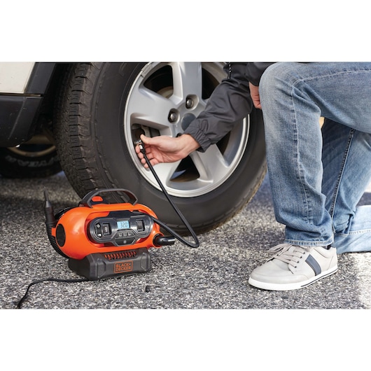 BLACKDECKER BDINF20 portable air inflator in use inflating a car tire on pavement.