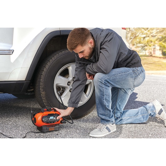 BLACKDECKER BDINF20 portable air compressor used to inflate a car tire on pavement.