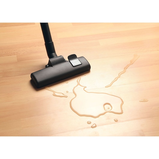 BLACKDECKER BDWDS20 vacuum nozzle cleaning liquid spill on light wood floor, top-down angle.