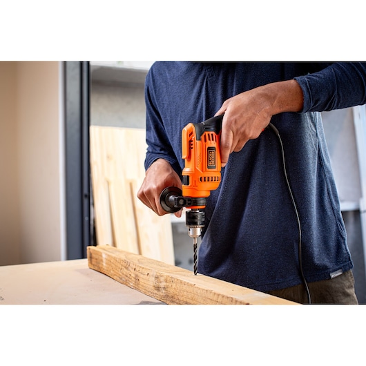 Photo of BLACKDECKER BED713650 corded electric drill being used to drill into a wooden board indoors.