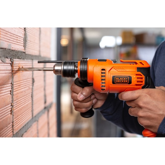 BLACK+DECKER BED713650 orange corded drill with side handle used to drill into brick wall.