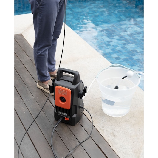 BLACKDECKER BEPW1300 pressure washer on deck beside pool with a water bucket and person standing nearby.