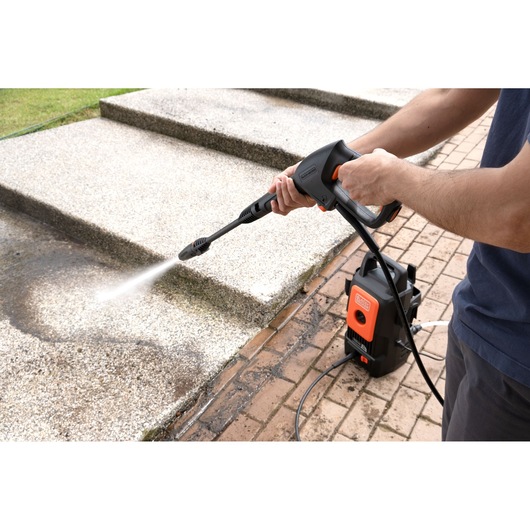 BLACKDECKER BEPW1520 pressure washer used to clean outdoor stairs, visible water spray and compact black-orange unit.