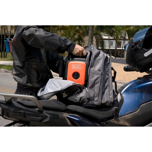 BLACKDECKER BEPW1520 portable pressure washer being placed in a gray backpack on a motorcycle seat outdoors.