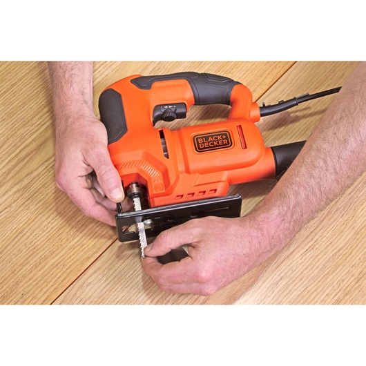 Photo of a BLACK+DECKER BES603 jigsaw on a wooden surface with hands installing the blade.