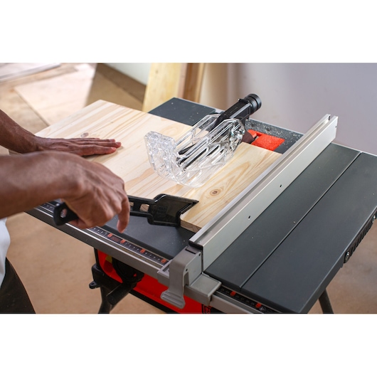 Photo of BLACKDECKER BES71800TSS table saw with wood plank being cut, showing hands guiding the material in workshop.