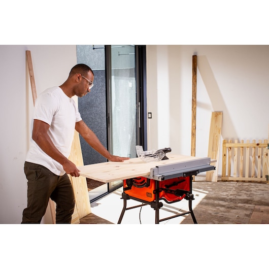 BLACKDECKER BES71800TSS table saw in use, cutting wooden board indoors, visible stand and safety guard.