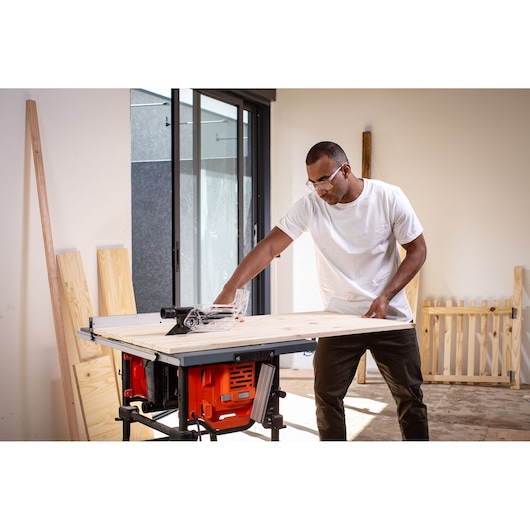Photo of a person using a BLACKDECKER table saw BES71800TSS to cut wood indoors.
