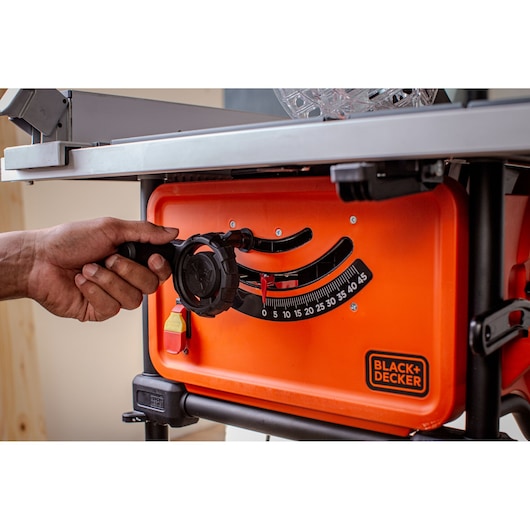 Photo of BLACK+DECKER BES71800TSS table saw side angle, showing hand adjusting bevel angle control knob.