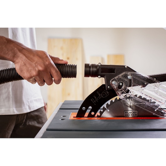 BLACK+DECKER BES71800TSS table saw with a hand connecting a vacuum hose to the blade guard, close-up angle.