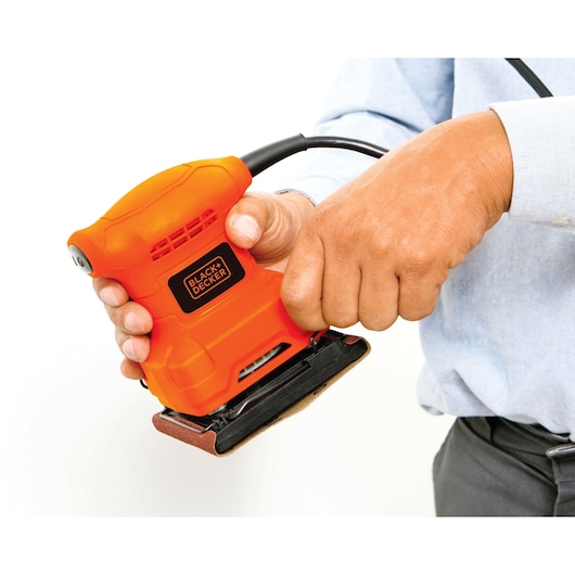 Photo of a BLACKDECKER BS200 orange palm sander being held in hand, close-up view, white background.