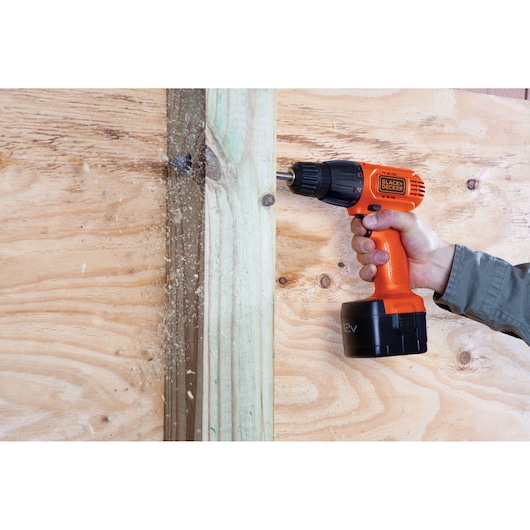 Photo of BLACKDECKER CD121K orange cordless drill in use, drilling into wood, hand holding the tool.