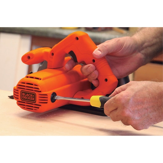 Photo of BLACKDECKER CS1004 power tool being adjusted with a screwdriver, visible hands, orange casing.