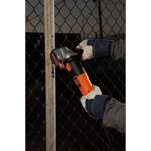 Photo of BLACKDECKER G720 angle grinder in use on a metal pipe, worker wearing gloves and denim protective sleeves.