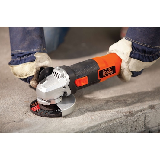 BLACK+DECKER G720 angle grinder in use on concrete, worker wearing gloves and denim sleeves.