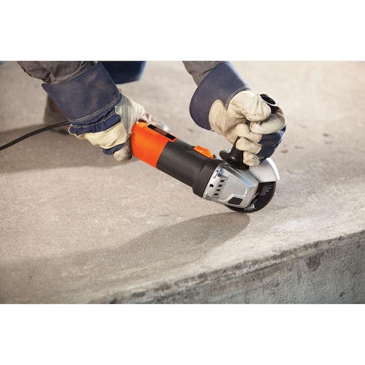 BLACKDECKER G720 angle grinder used on concrete, orange and black body, worker wearing gloves.
