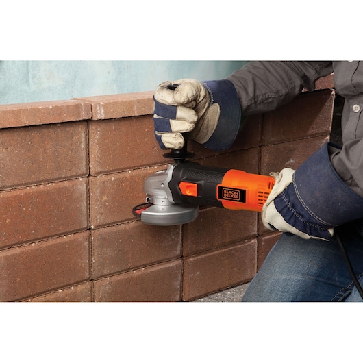 Photo of BLACKDECKER G720 angle grinder in use on brick wall, operated by gloved hands.