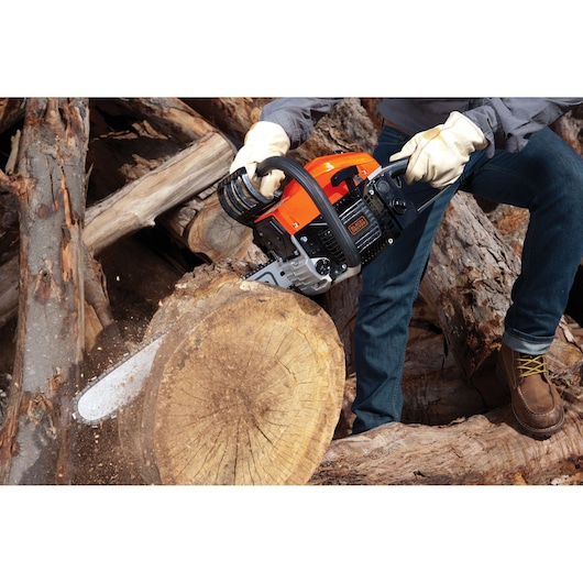 BLACKDECKER GGK45 chainsaw cutting tree log outdoors, operator wearing gloves and boots.
