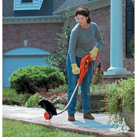 Photo of person using BLACKDECKER GH1100 electric string trimmer on garden pathway.
