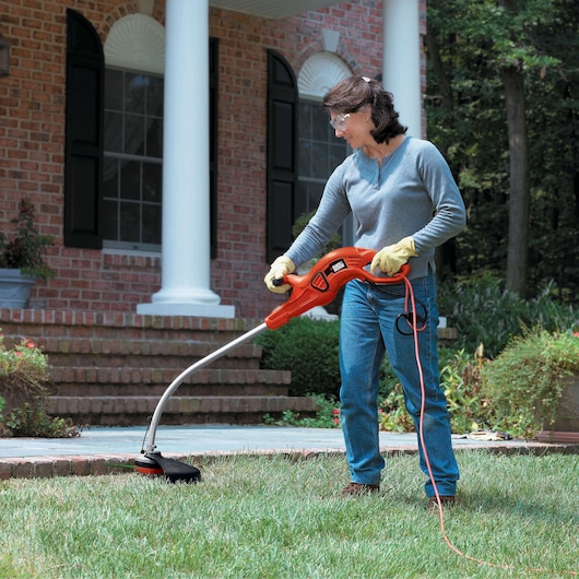 BLACKDECKER GH1100 string trimmer in use trimming grass near brick house, orange body, corded design.