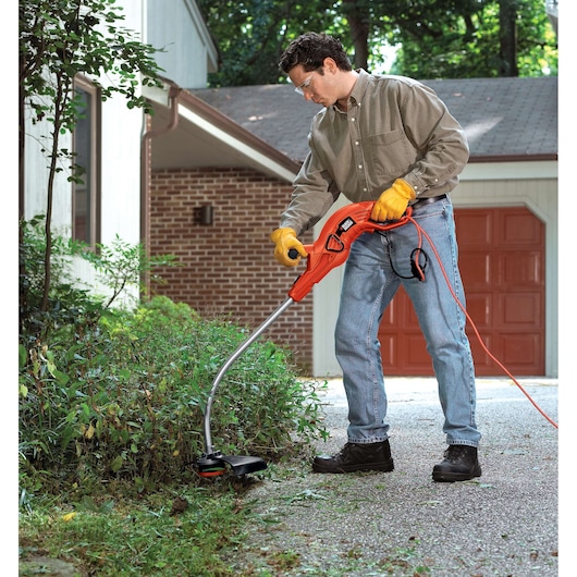 Photo of person using BLACKDECKER GH1100 orange electric string trimmer to edge garden near driveway.